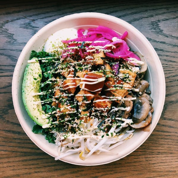A colorful poke bowl with tofu, avocado, kale, pickled onions, mushrooms, and bean sprouts.