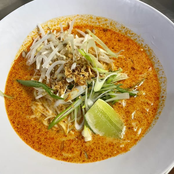 A Mighty Bowl laksa with bean sprouts, fried shallots, scallions, and a lime wedge.