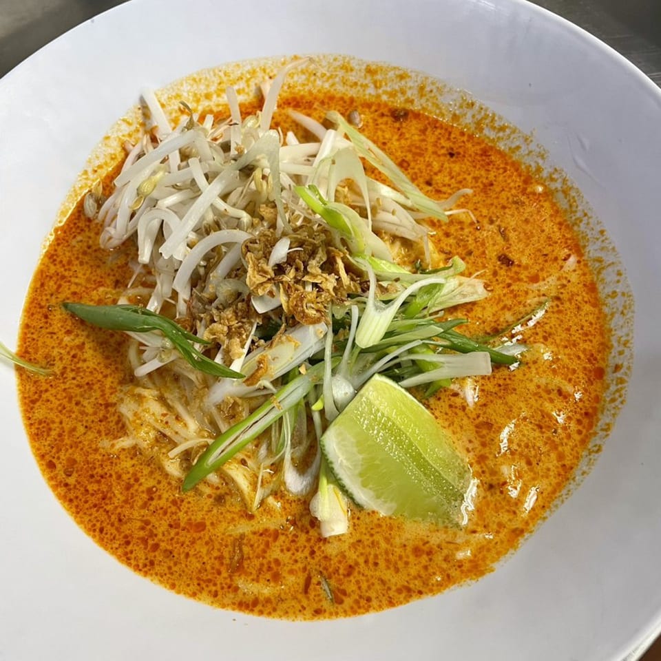 A Mighty Bowl laksa with bean sprouts, fried shallots, scallions, and a lime wedge.