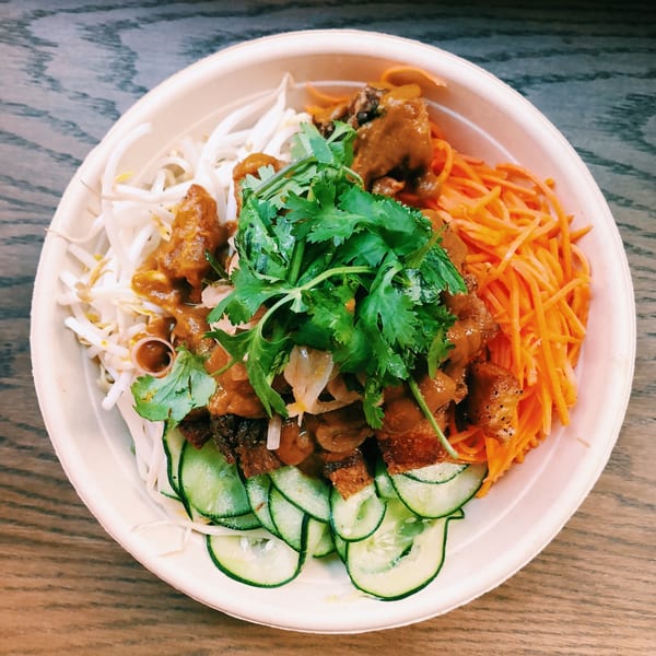 Mighty Bowl's Asian-fusion bowl with noodles, carrots, cucumbers, meat, and cilantro on a wooden table.